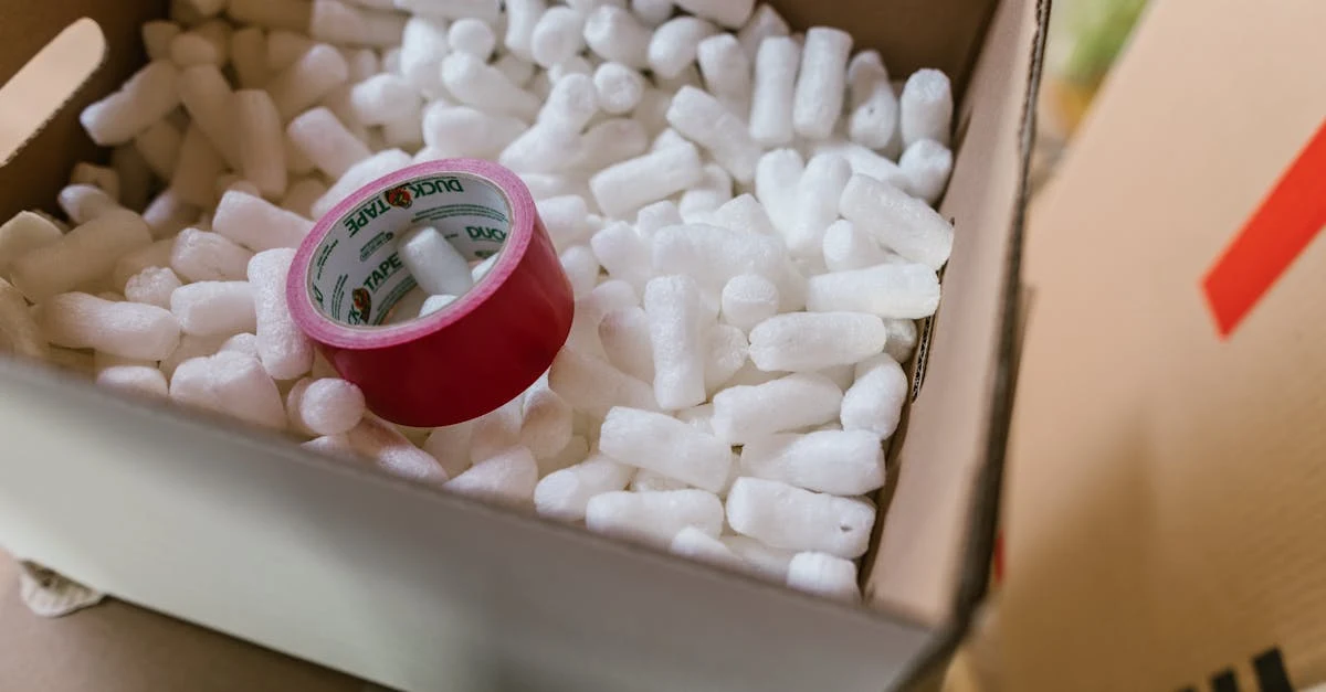 A cardboard box filled with white packing peanuts and a roll of red duct tape inside.