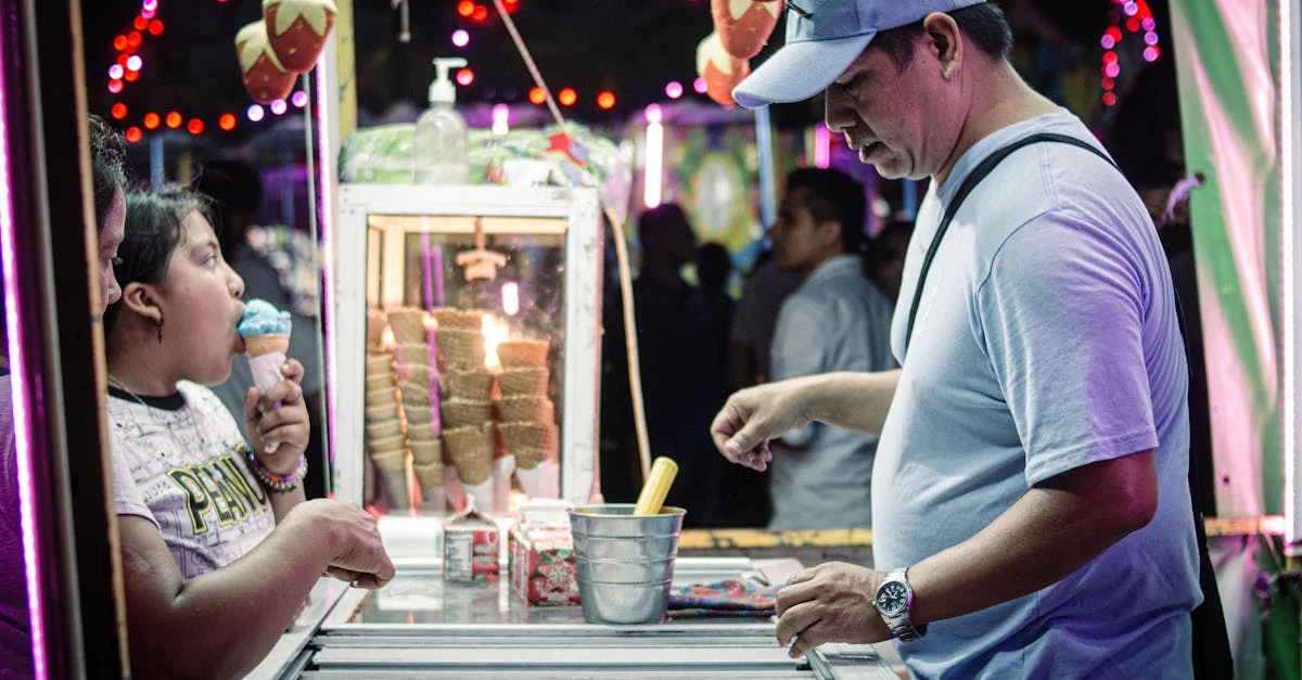 Vendor serving ice cream to customer at colorful fair stand with inventory management compostable products display.