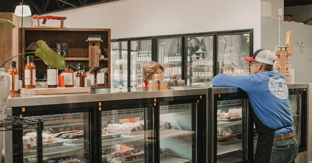 Bakery counter with glass-door refrigerated display cases showing pastries and baked goods, worker in blue shirt restocking.
