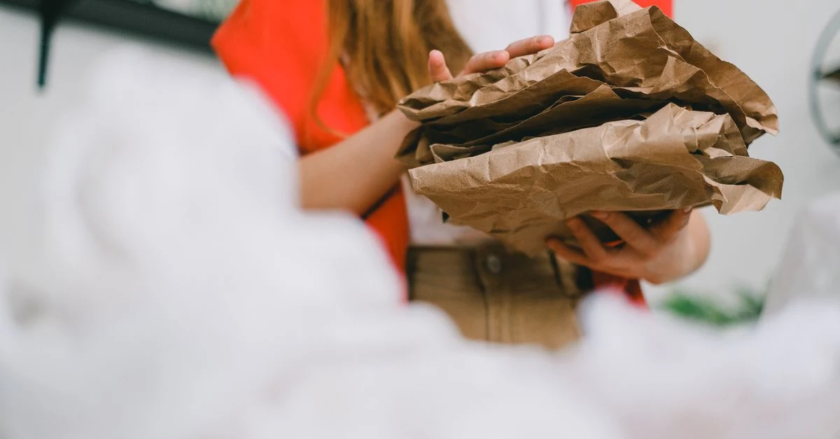 Person holding crumpled brown compostable packaging compared to traditional paper alternatives.