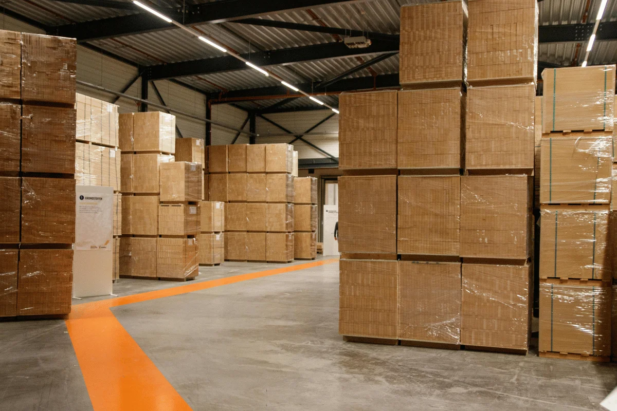 Stacks of cardboard boxes arranged in a spacious warehouse with high ceilings.
