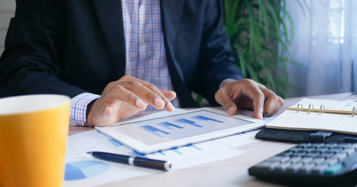 Professional reviewing sales data on tablet with financial charts and calculator for packaging business strategy.