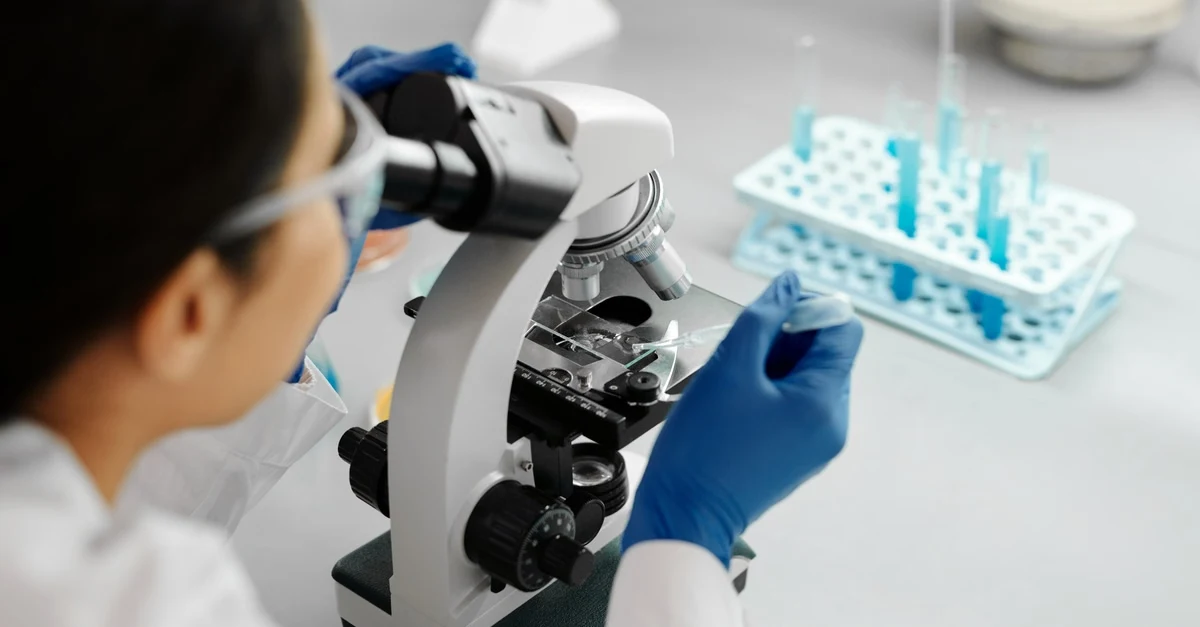 Scientist examining sample under microscope for PFAS-free testing and certification.