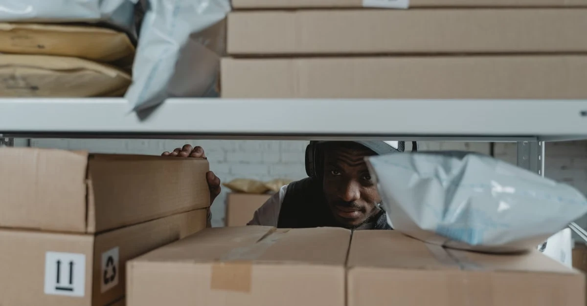 Man surrounded by cardboard boxes with recycling symbol, evaluating compostable packaging suppliers for business standards.