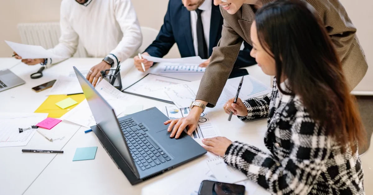 Diverse business team collaborating around laptop and documents, selecting compostable packaging suppliers for growth.