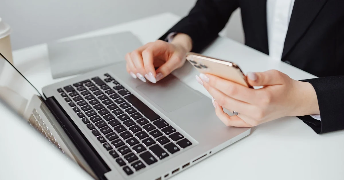 Woman examining smartphone and laptop, verifying compostable packaging supplier certifications.