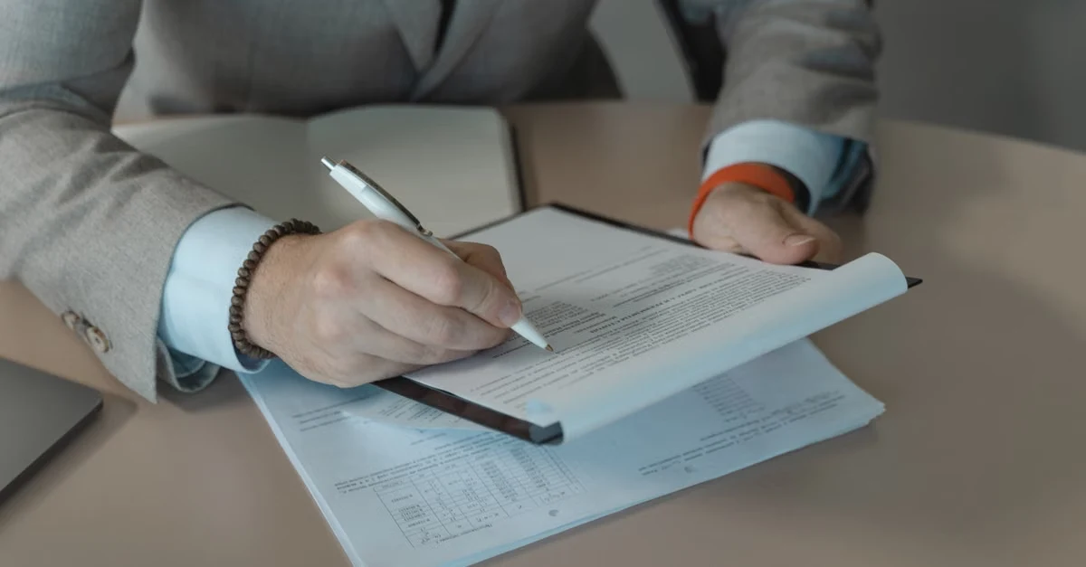 Professional reviewing supplier contract documents at desk while taking notes on compostable products sourcing.