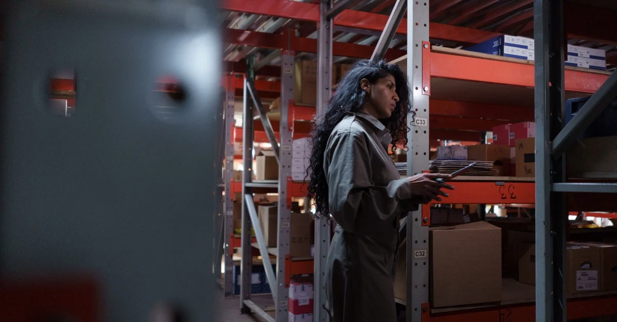 Warehouse worker checking inventory on red industrial shelving for sustainable distributor operations.