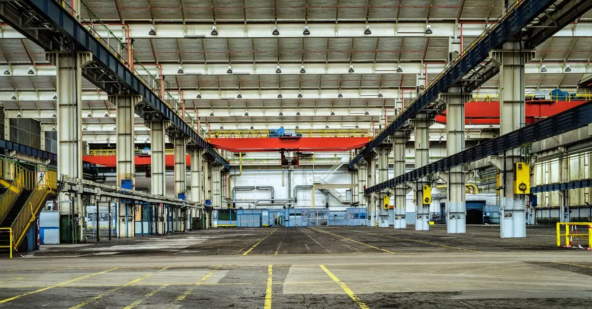 Industrial warehouse with overhead cranes and yellow safety lines for compostable products sourcing and logistics operations.