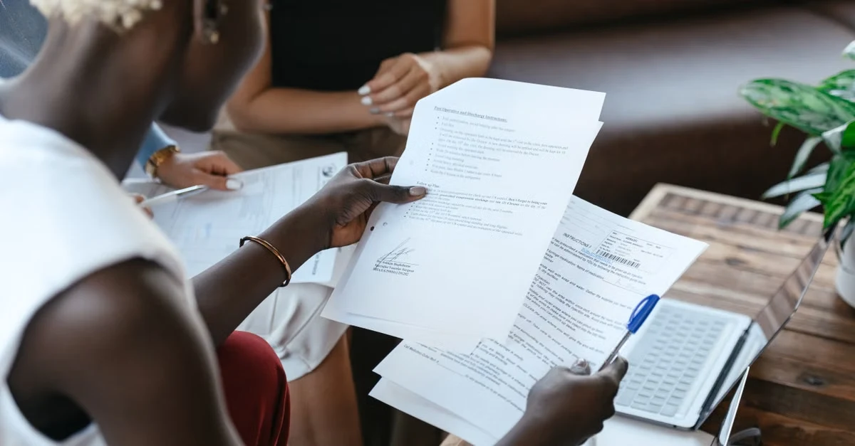  Two people reviewing supplier certification verification documents at a wooden table indoors.