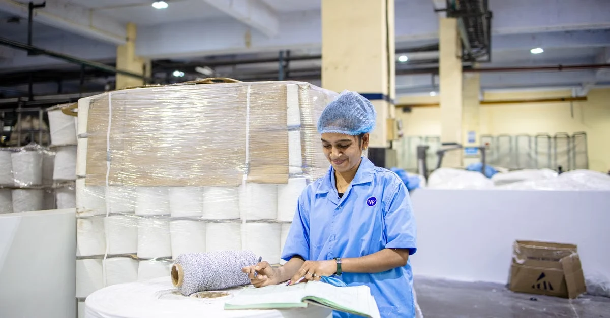 Worker in blue uniform inspecting rolled compostable products sourcing materials in manufacturing warehouse facility.