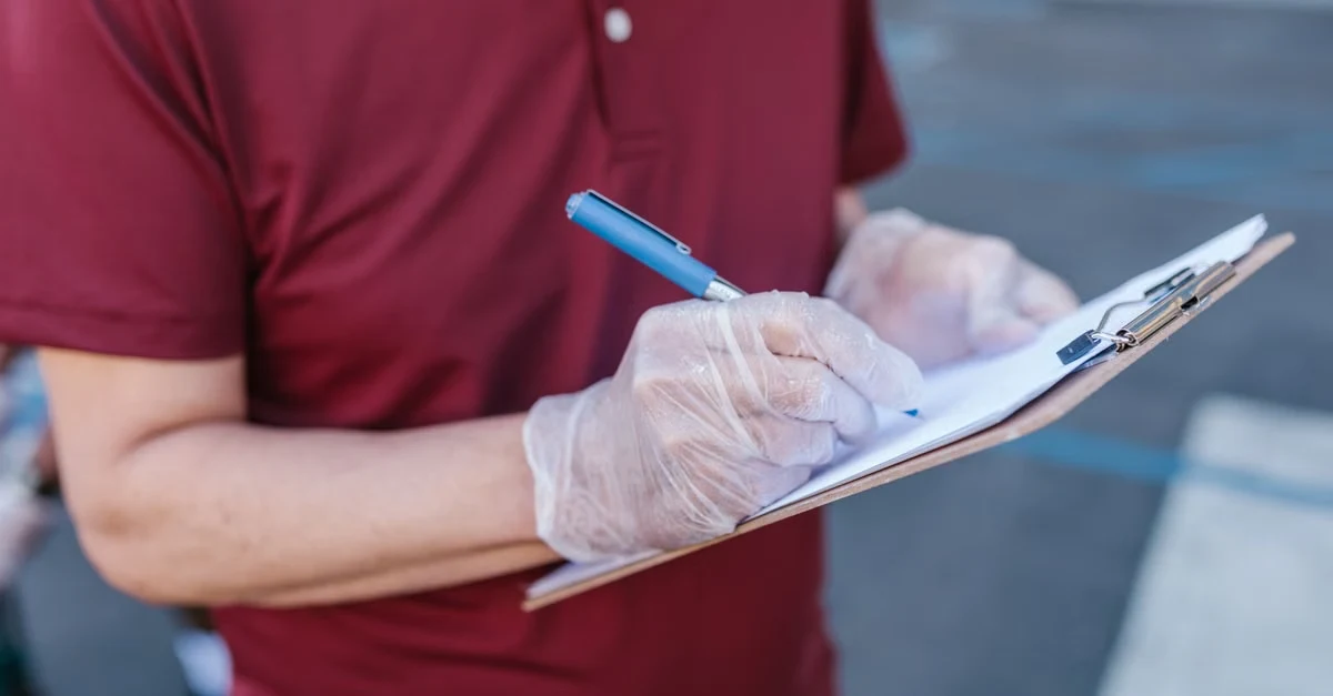Worker in maroon shirt wearing white gloves holding clipboard and pen for compostable packaging suppliers audit.