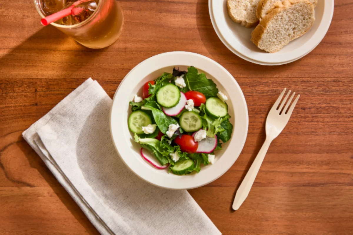Fresh salad with bread, iced drink, and disposable fork on a wooden table using NantBR products.