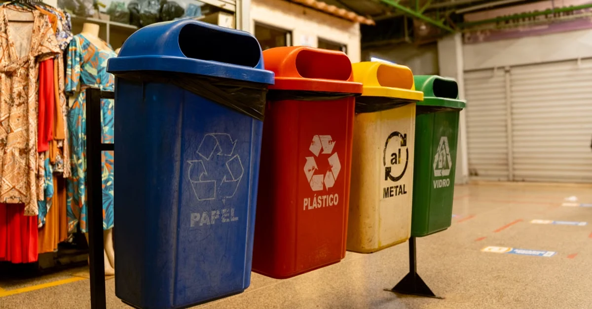 Four separate recycling and composting solutions bins labeled papel, plástico, metal, and vidrio in warehouse.