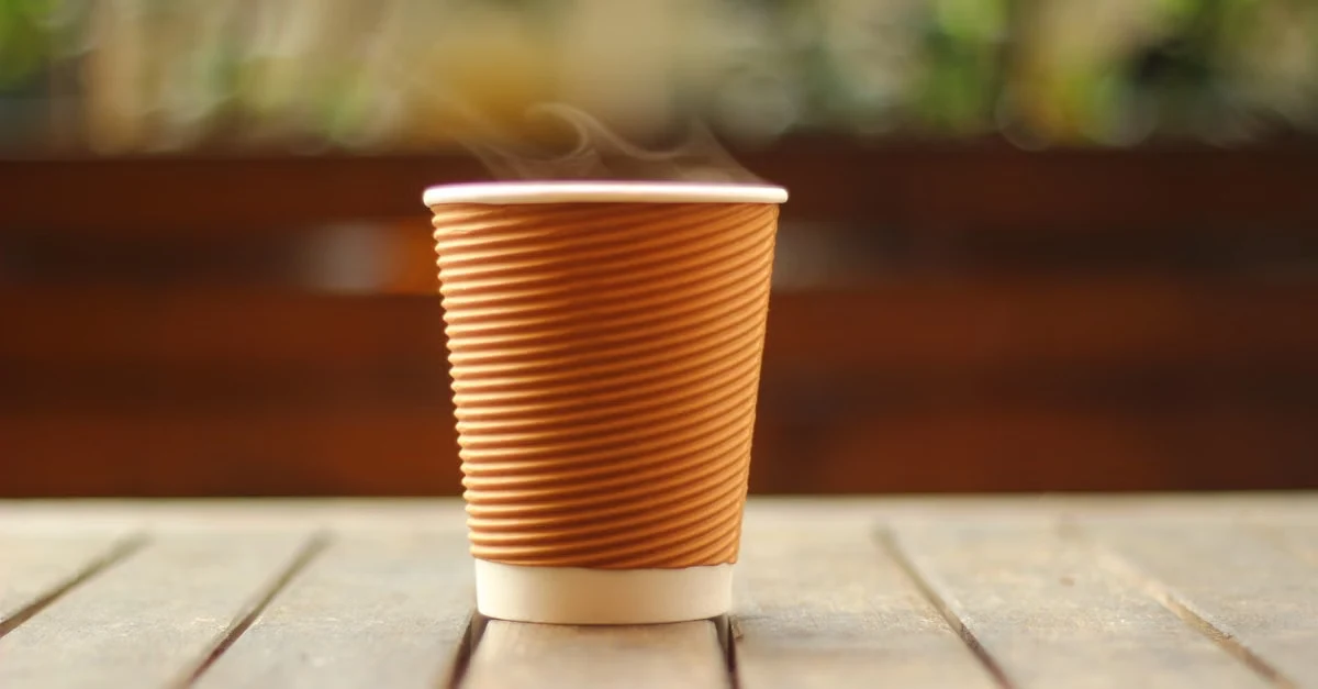 Brown ridged compostable material selection cup on wooden surface with blurred garden background.
