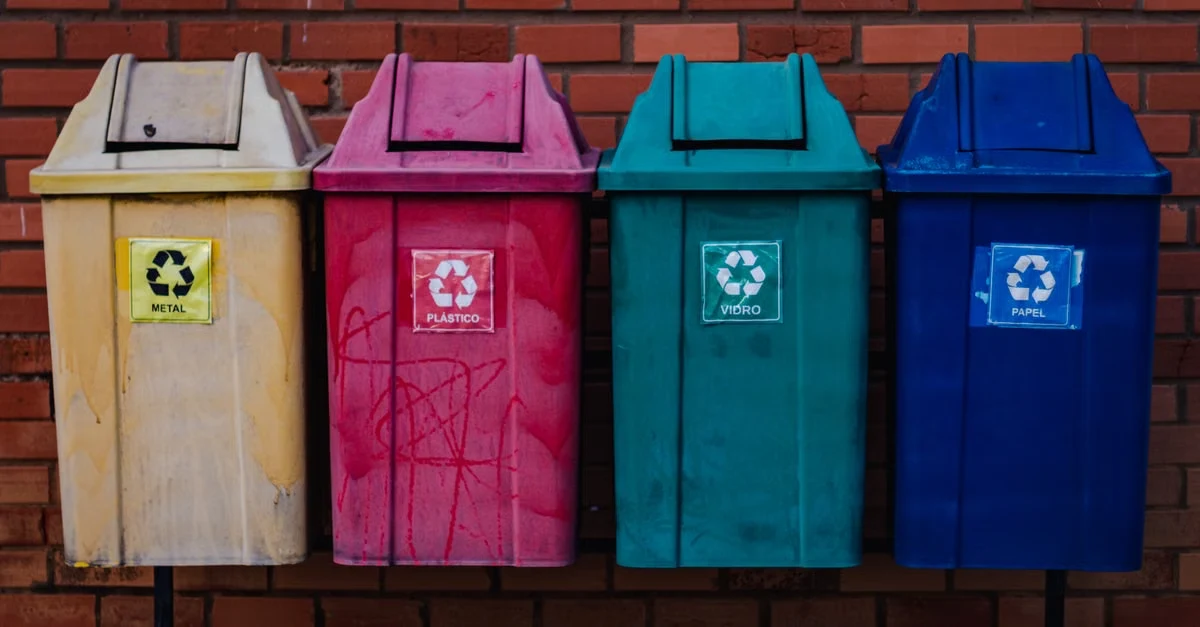 Four color-coded recycling bins with metal sorting labels against red brick, showing limited compostable straws municipal.