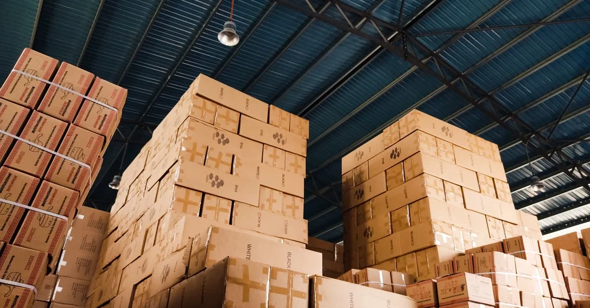 Stacked cardboard boxes in warehouse showing compostable packaging certifications labels and markings on storage shelves.