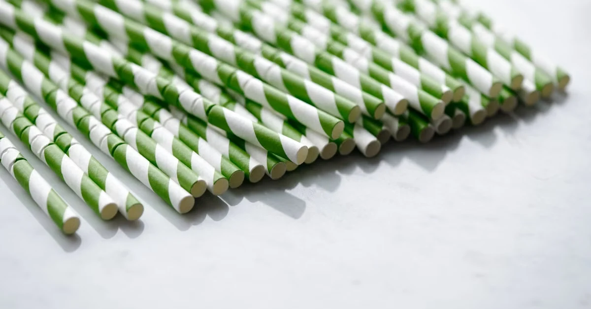 Rows of green and white striped compostable straws arranged neatly for municipal composting disposal.