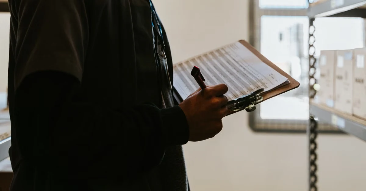Person holding clipboard with lined checklist near shelving, reviewing compostable packaging certifications requirements.