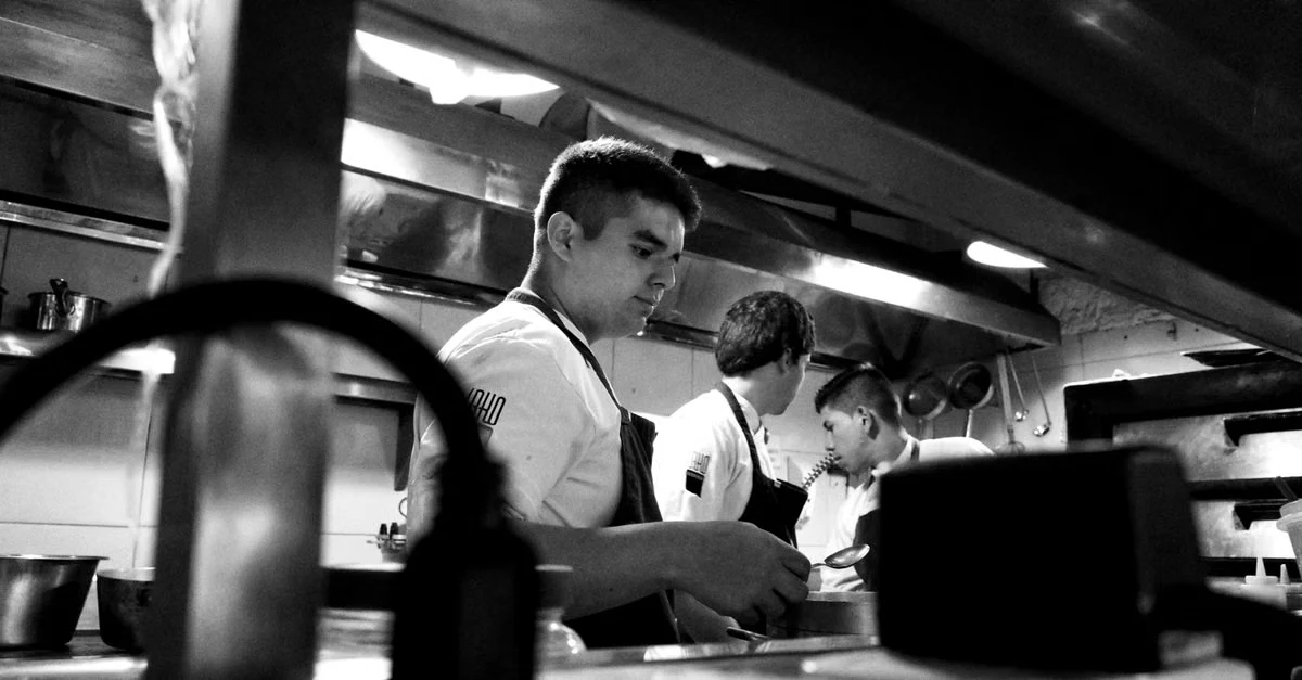 Professional kitchen staff working at composting infrastructure foodservice station with equipment and containers visible.